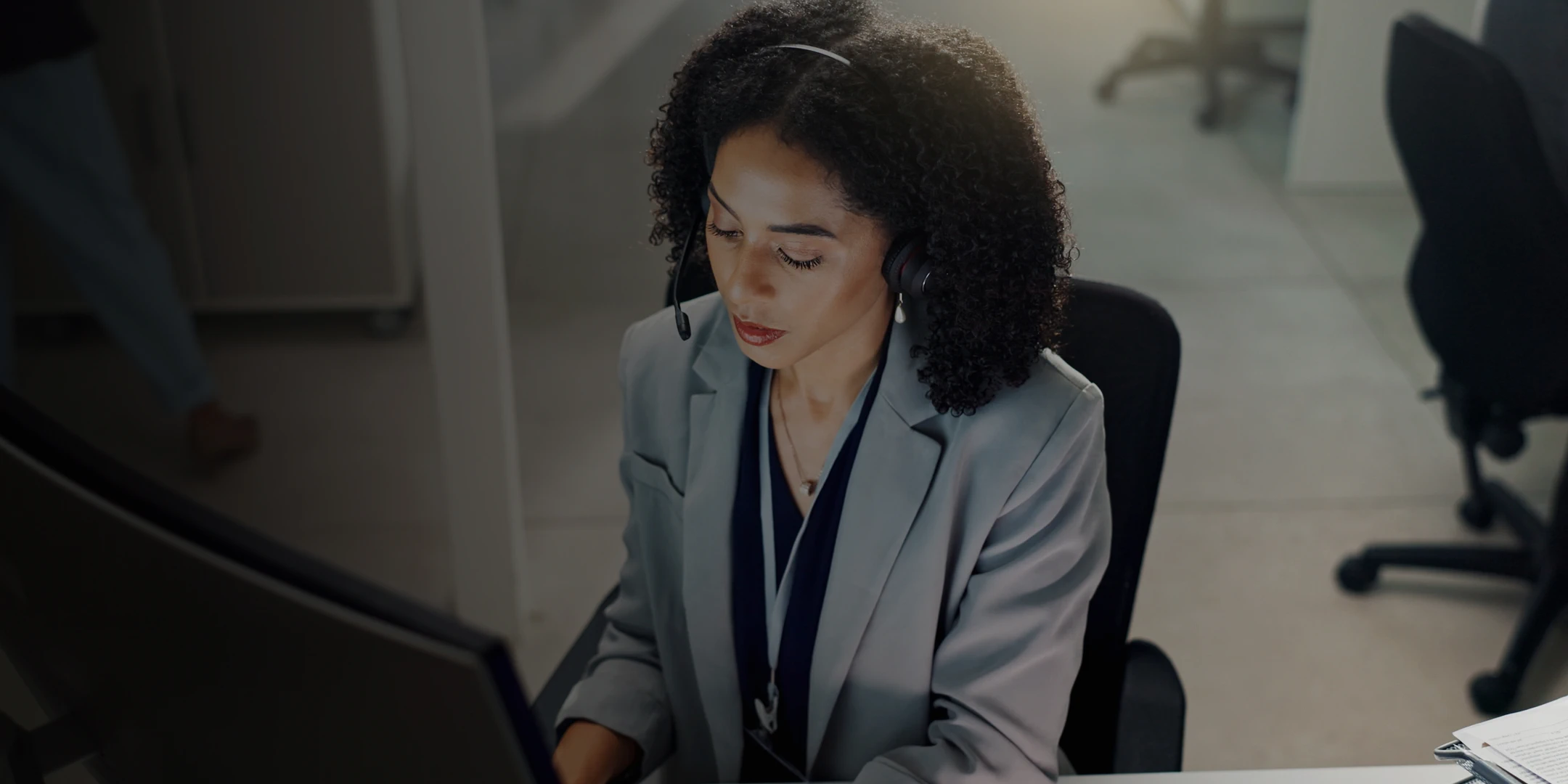 Woman in a blazer with a headset, providing customer support at her desk.