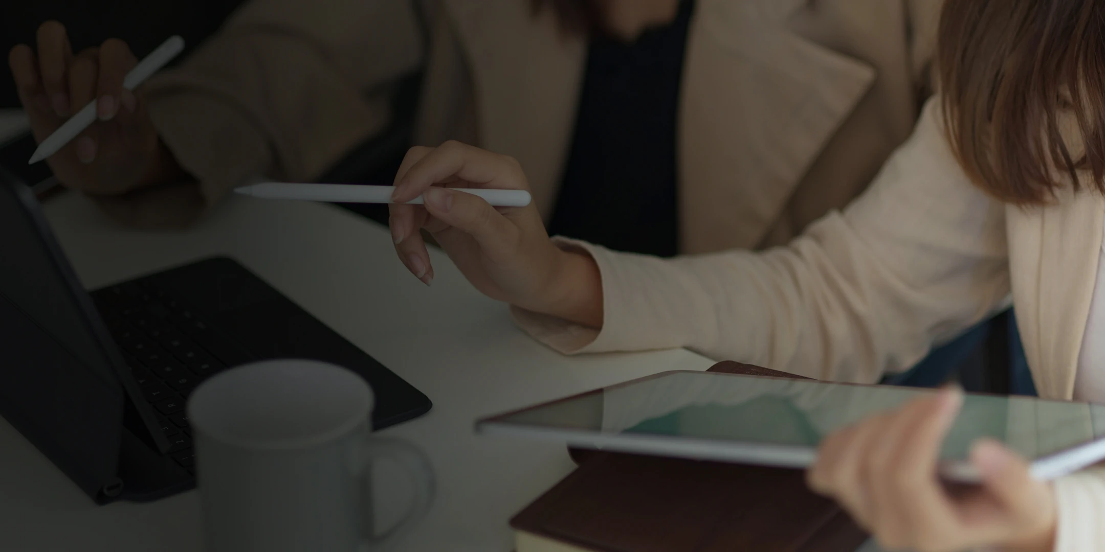 Two people dressed in business suits are working at a table, using styluses and tablets.