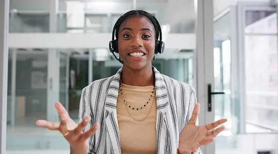 Customer support agent wearing a headset, gesturing with open hands.