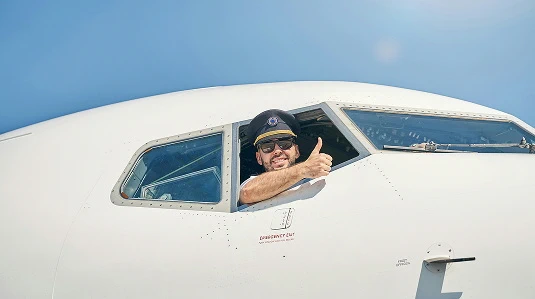 Man in pilot uniform giving a thumbs up inside an airplane cockpit