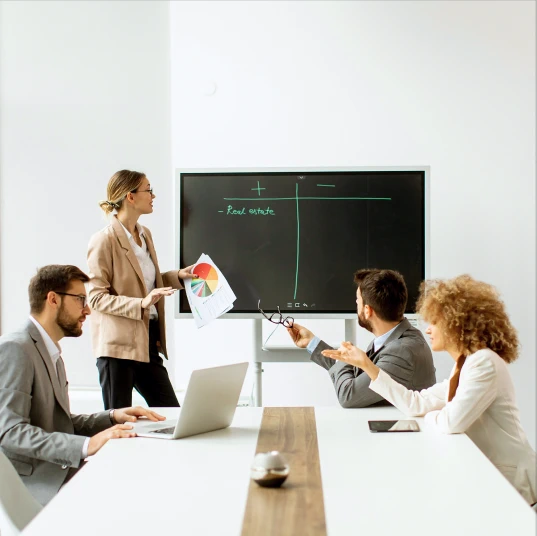 Team of people in a meeting with a pie chart and whiteboard presentation.