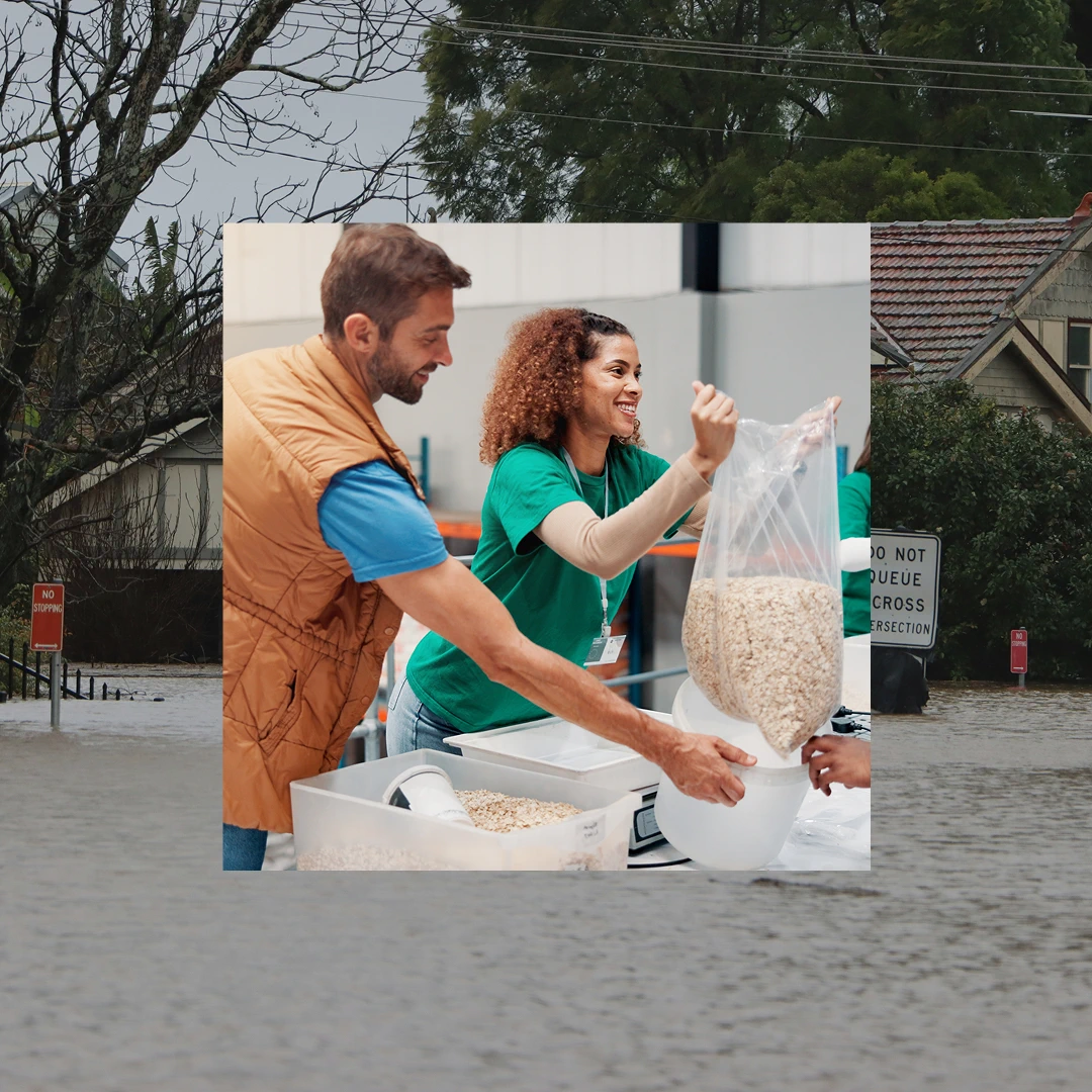 Two volunteers in green shirts preparing food: a man scooping into a container and a woman lifting a bag of oats