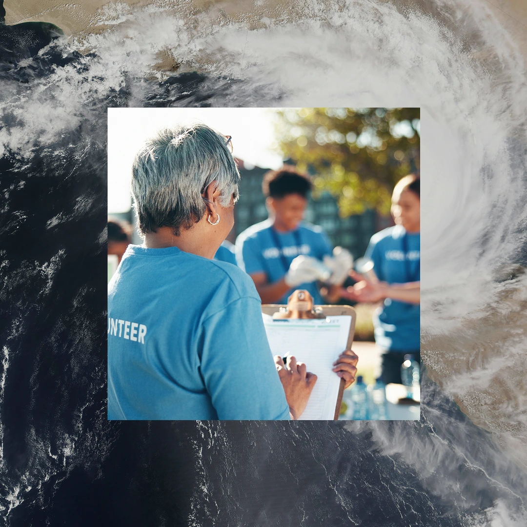Back view of a woman wearing a "Volunteer" t-shirt, holding a clipboard and overseeing a group of volunteers