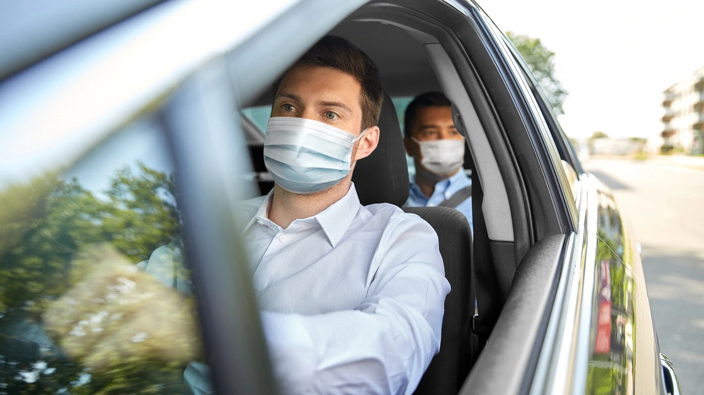 Two men, a driver and a passenger inside a car, both wearing medical masks