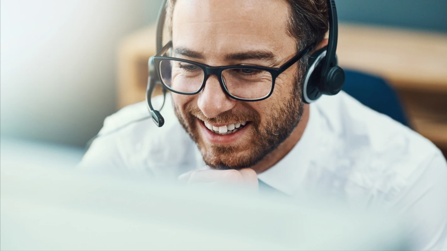 Friendly, engaging customer service representative with headset and white shirt, looking at a computer screen