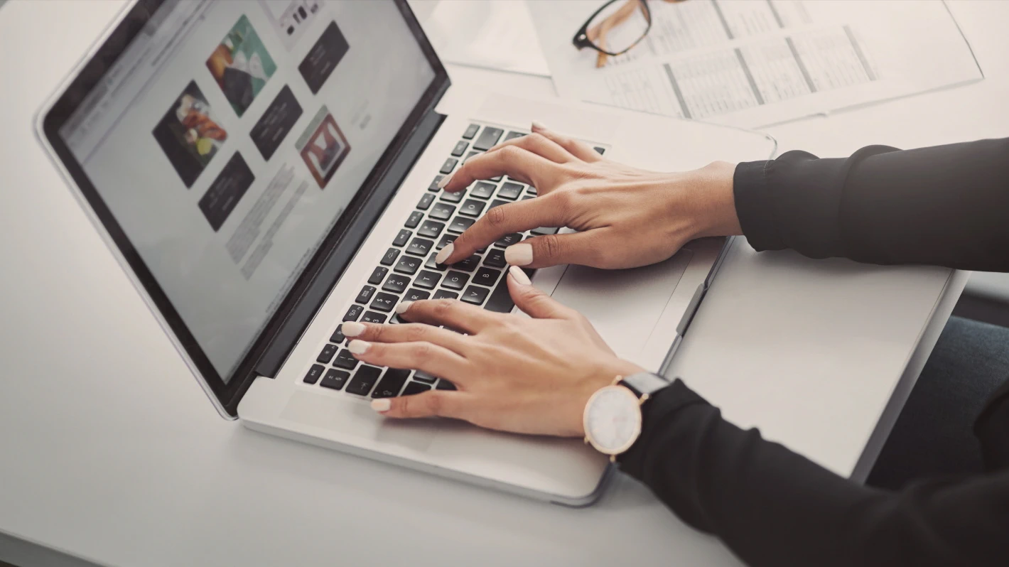 Close-up shot of a person working on a laptop, hands typing on the keyboard