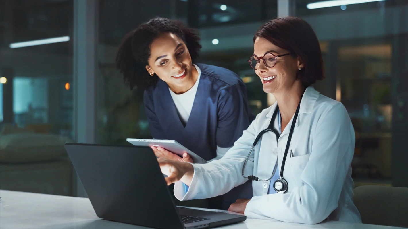 Medical professionals collaborate by reviewing a laptop and tablet in a modern office