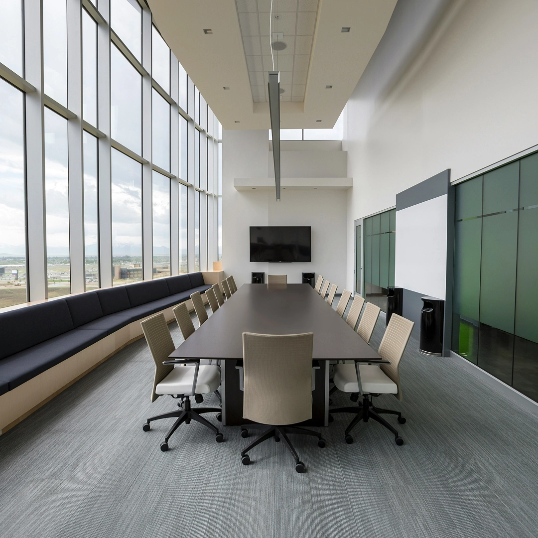 Spacious conference room with floor-to-ceiling windows, a long table, and a large screen