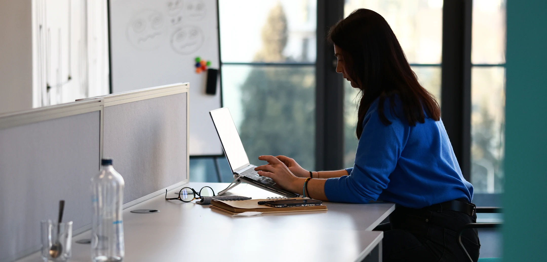 Woman with dark hair, wearing a blue blouse, working on a laptop at a desk
