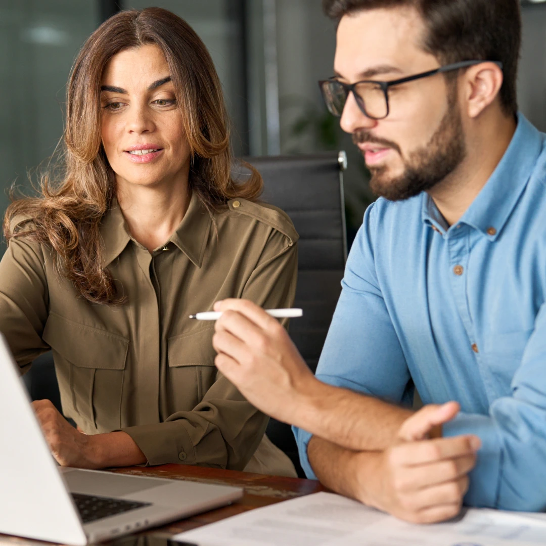 Male and female call center representatives in Poland collaborating at a table and looking at a laptop screen.