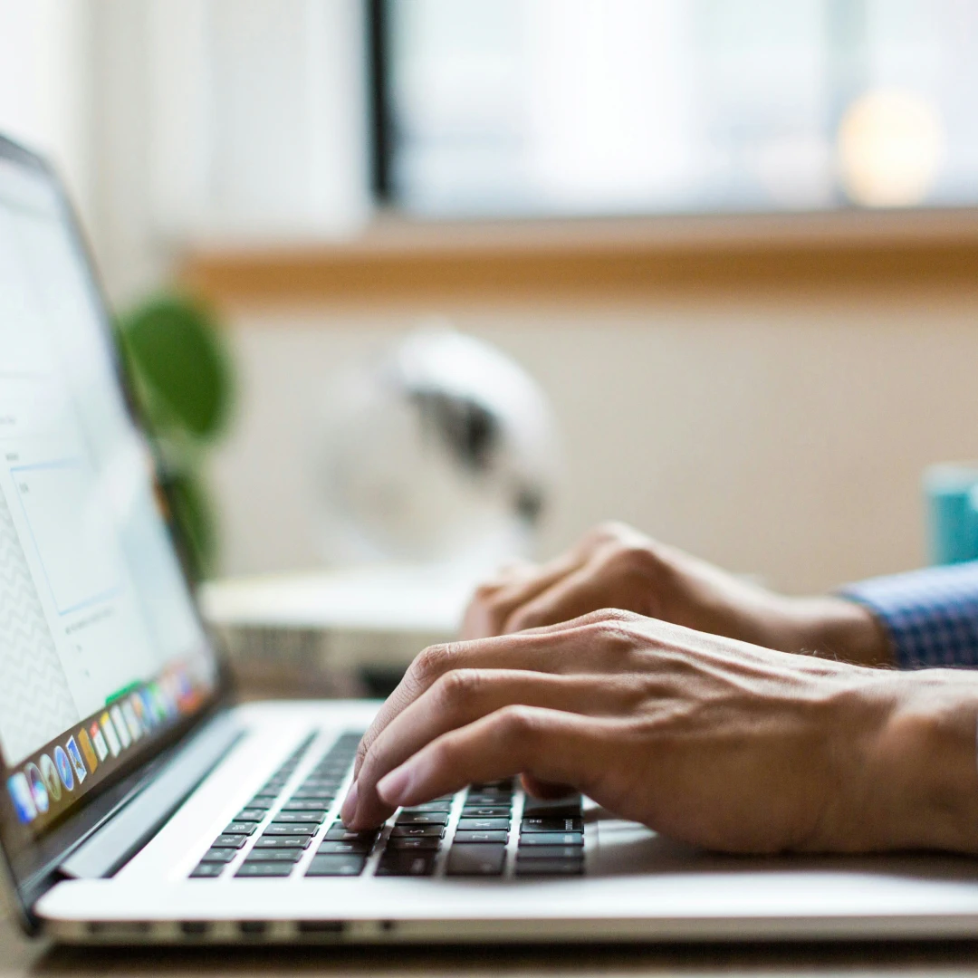 Close-up of hands typing on a silver laptop