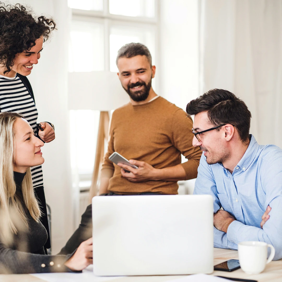 People collaborating around a laptop in a bright, modern office environment