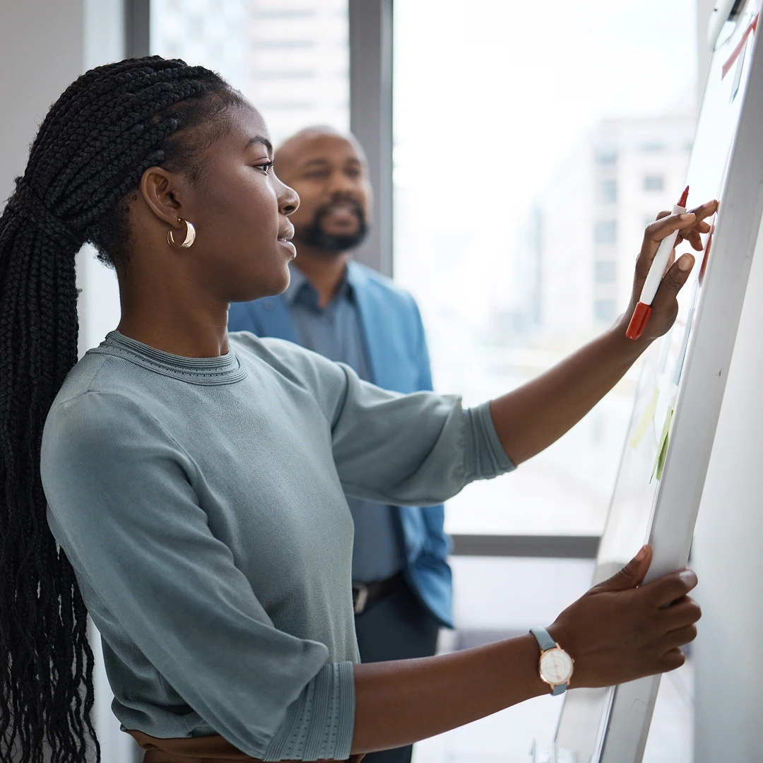 Woman with long black hair in a green shirt presenting on a whiteboard