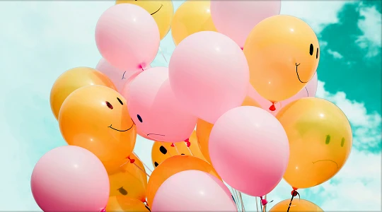 Pink and yellow balloons with smiley faces against a blue sky