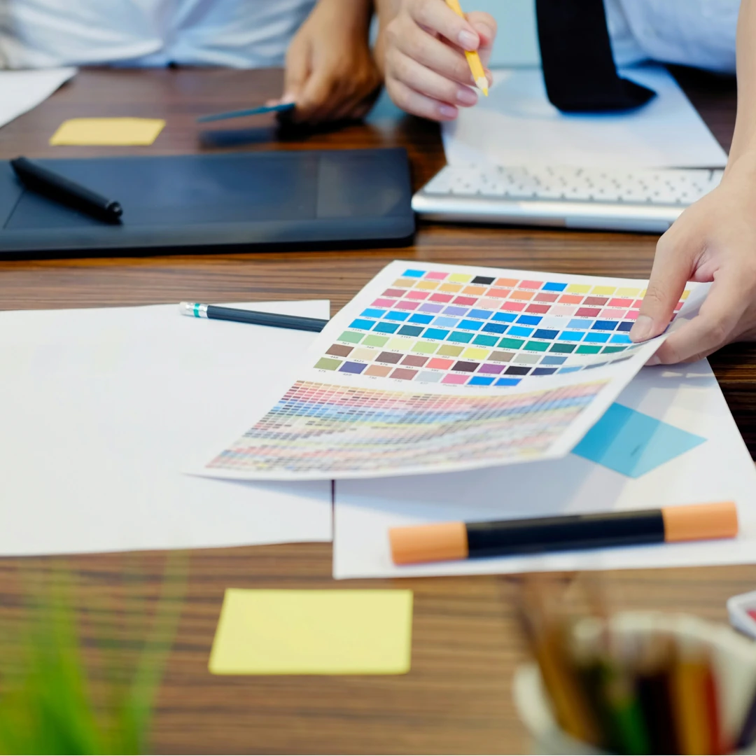 Close-up of hands holding documents at a desk with a laptop, keyboard, and pens