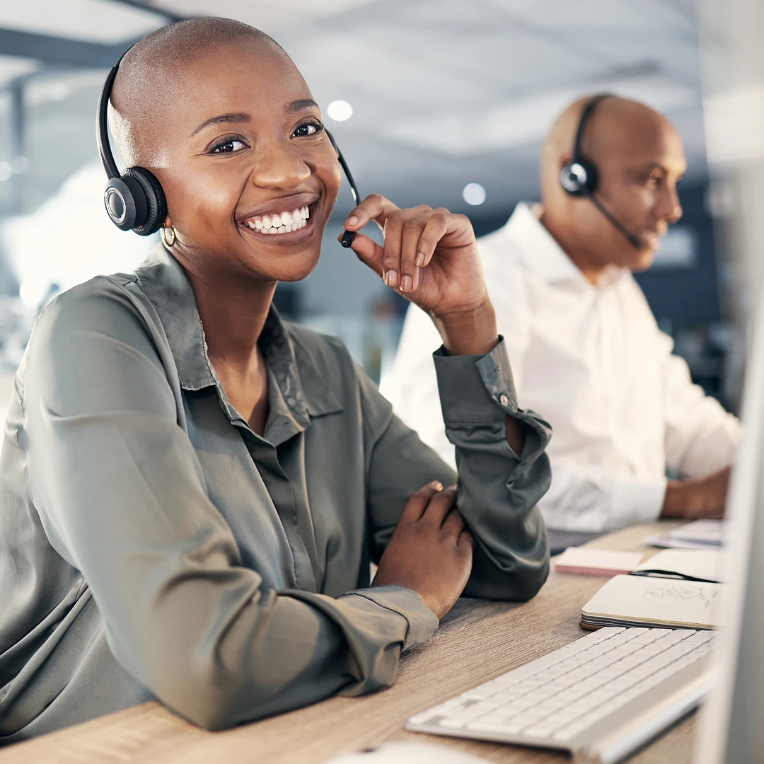 Smiling customer support agents wearing grey and white shirts and headsets, ready to assist.