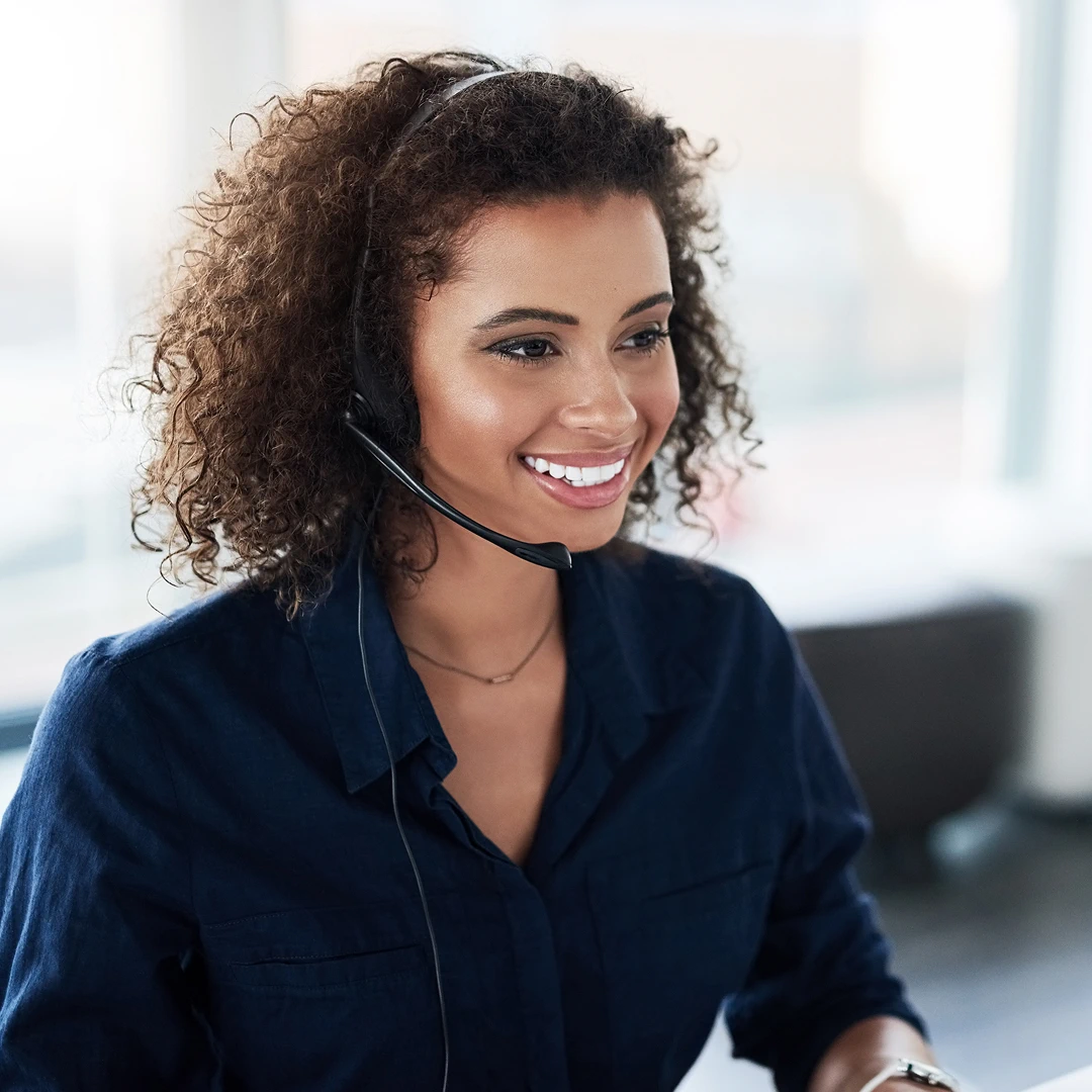 Female customer support agent with curly hair and a warm smile, wearing a headset