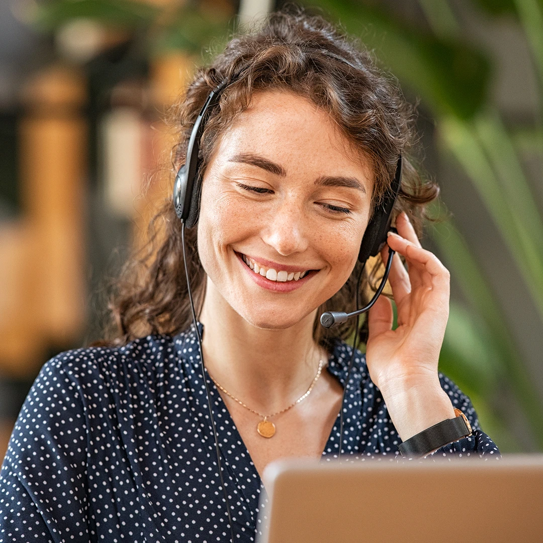 Smiling female customer support agent with a headset and curly hair assisting a client
