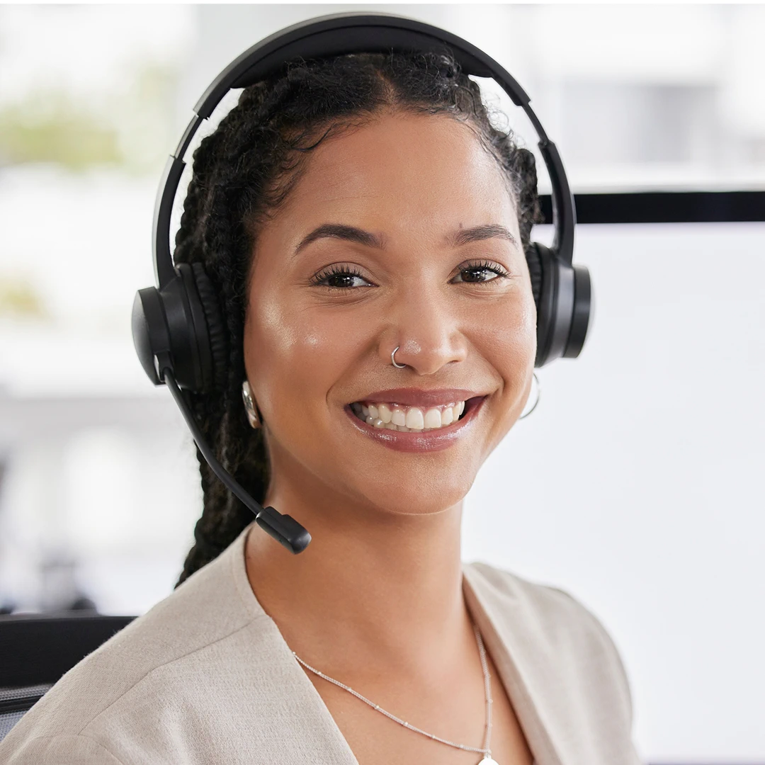 Smiling female customer support agent wearing white blazer with black braided hair, headset, and nose ring