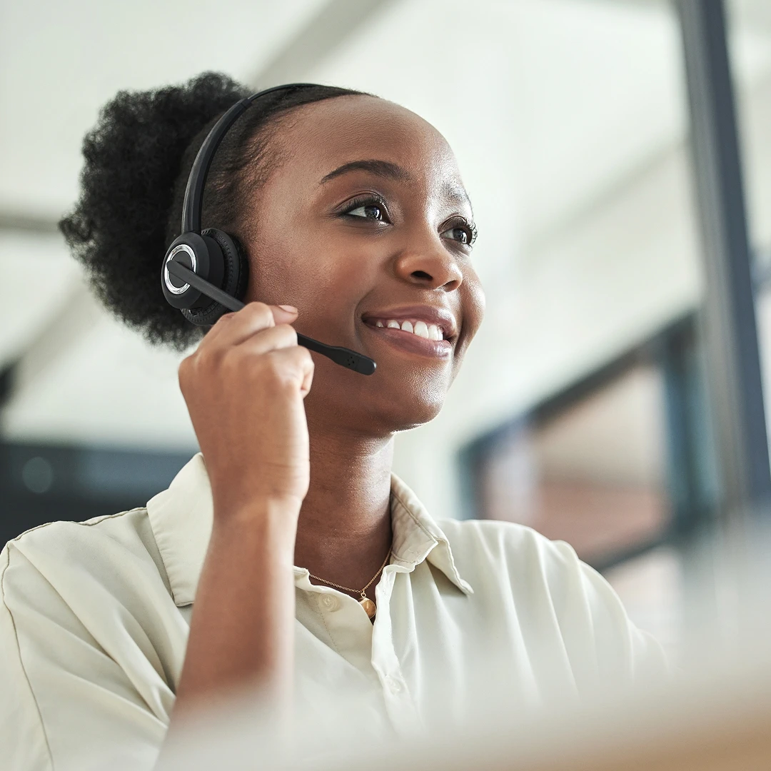Friendly and helpful female customer support representative with long curly black hair, wearing a headset and a white shirt