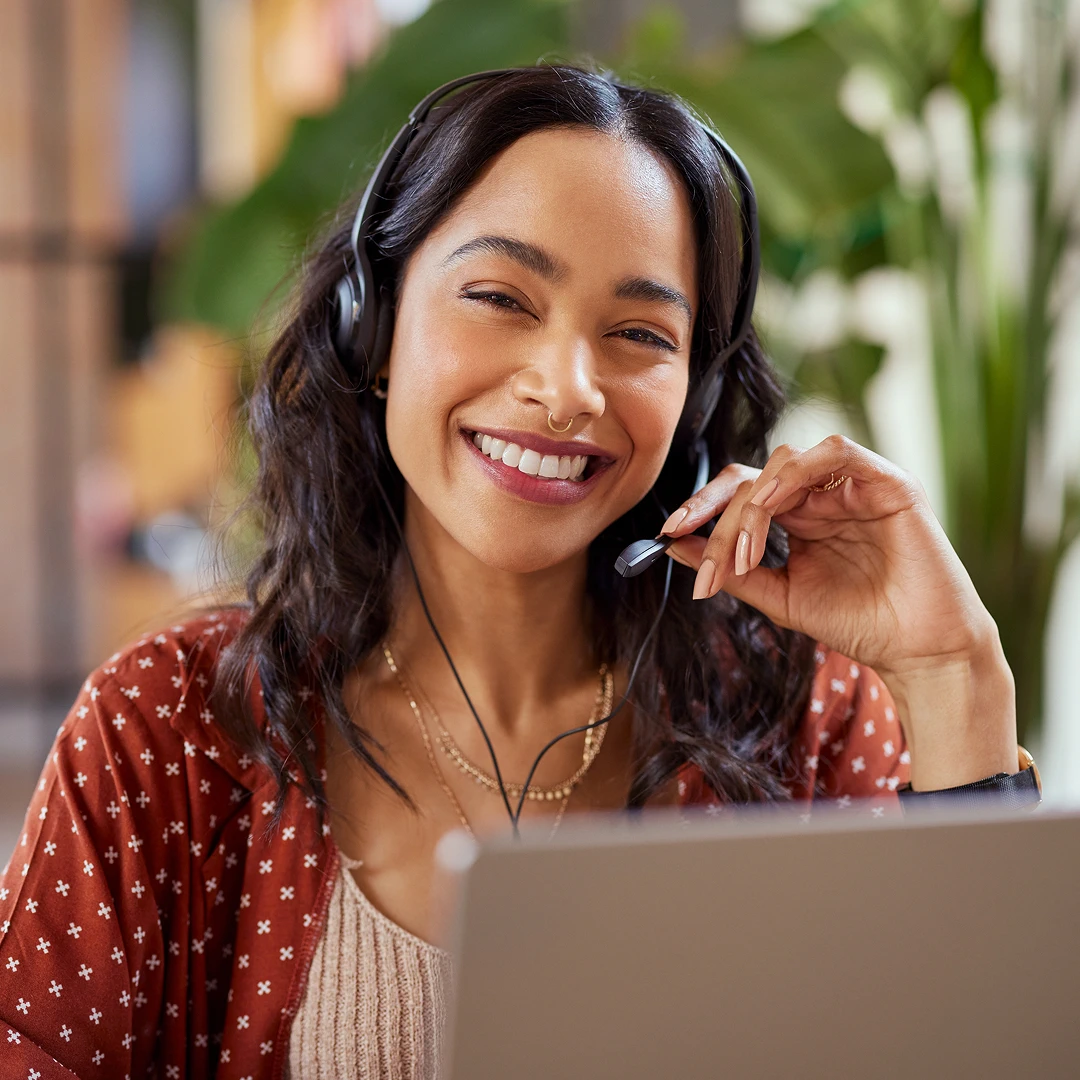 A smiling woman with dark hair and a nose ring, wearing a headset, providing customer support