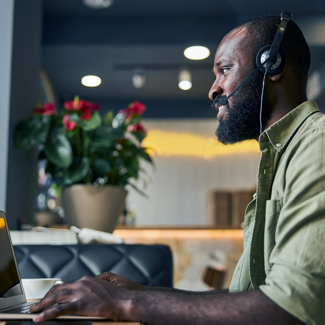 Male customer support agent in a light green shirt with a headset working at his workstation