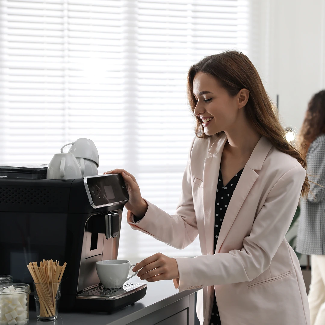 A woman is smiling, making coffee from the coffee machine in the office