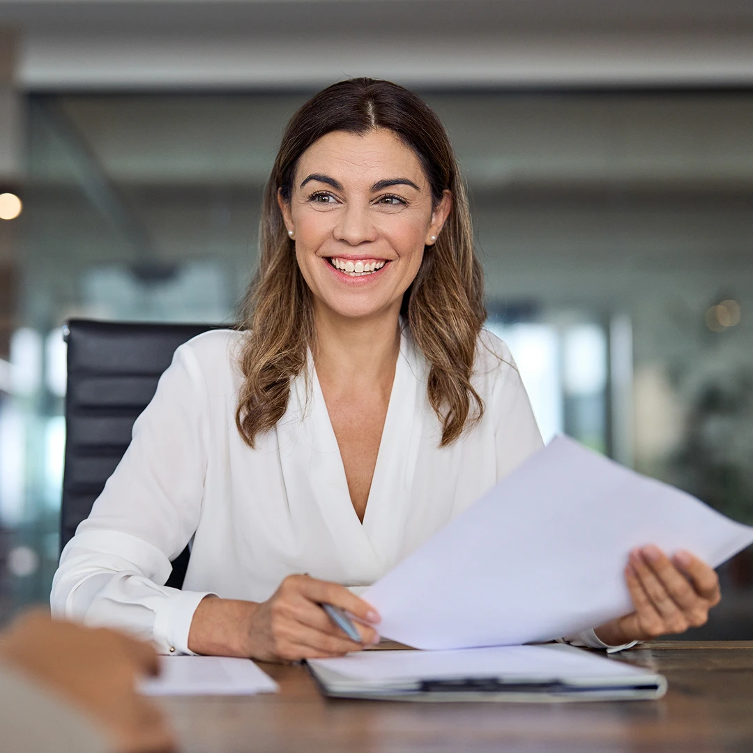 Smiling businesswoman with long brown hair sitting at a table and holding documents in a Polish call center office