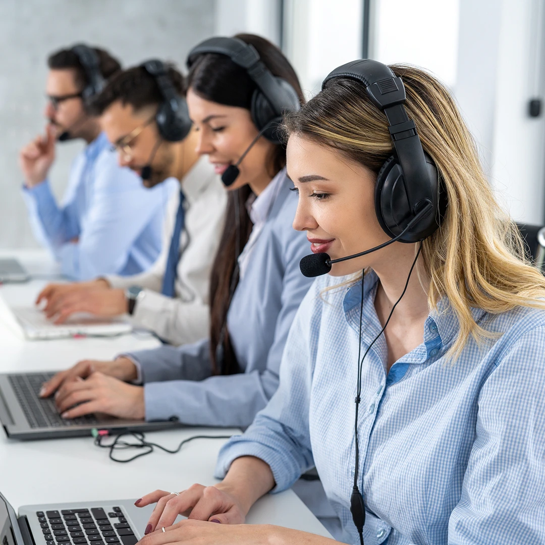 Diverse financial customer service agents in blue shirts wearing headsets, working on laptops at a white office desk