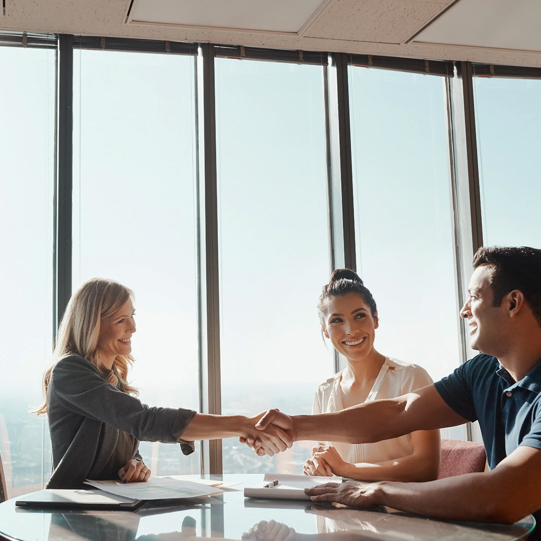 People in a business agreement are smiling. One is shown shaking another’s hand in agreement