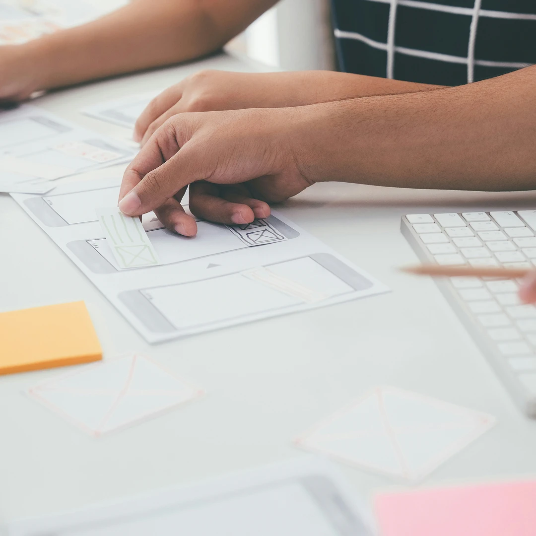 Close-up of two people's hands working on a design on a white sheet of paper