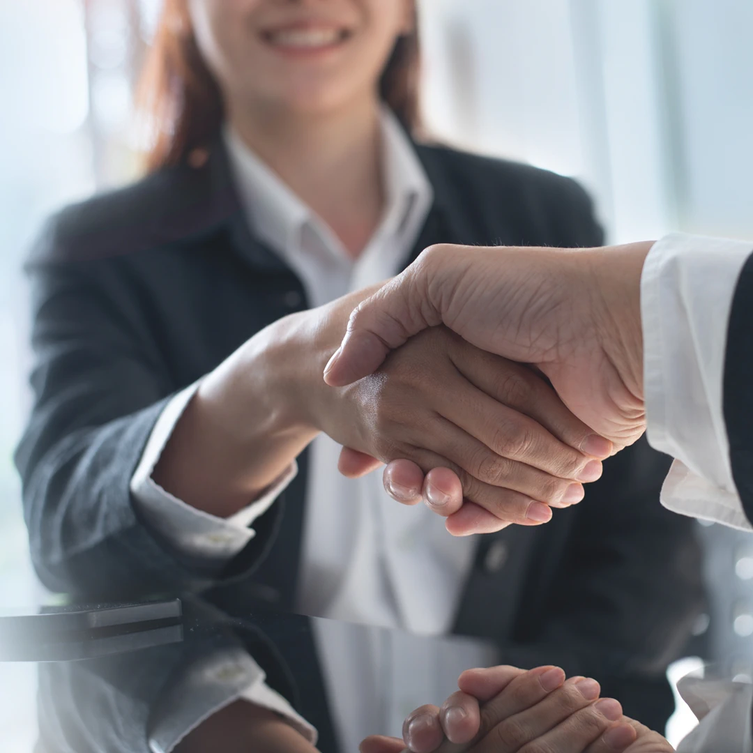Two business people in formal suits shaking hands in a modern office