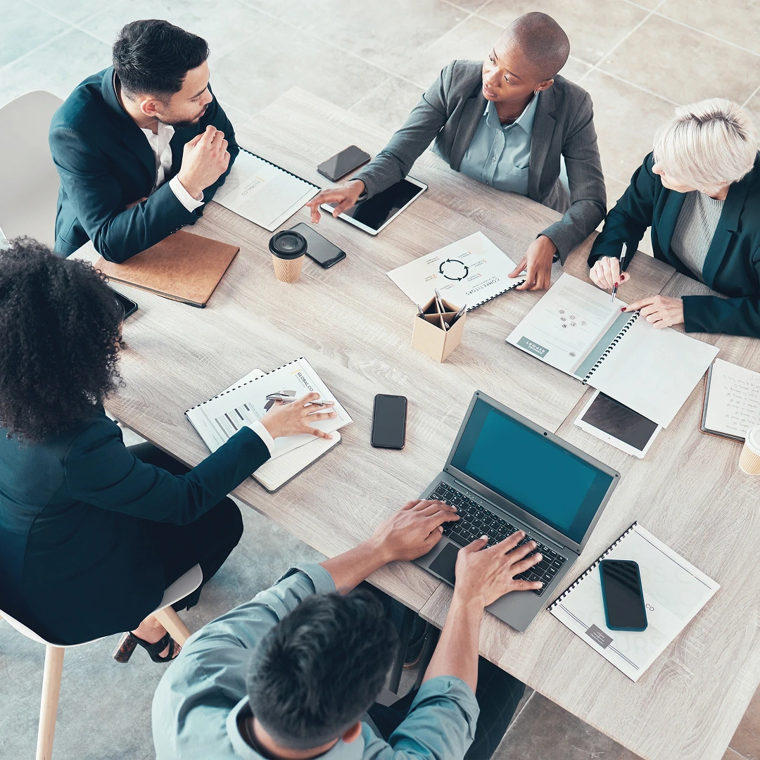 Group of professionals collaborating around a table with documents, laptops, and mobile devices
