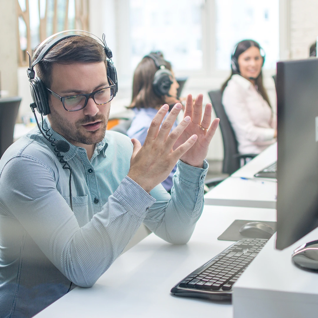 Customer service representative wearing a headset and light blue shirt, gesturing while providing phone support