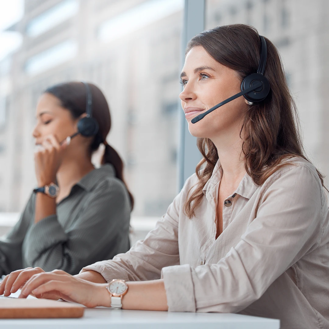 Two professional healthcare call center agents wearing headsets, working together in a bright, modern office space