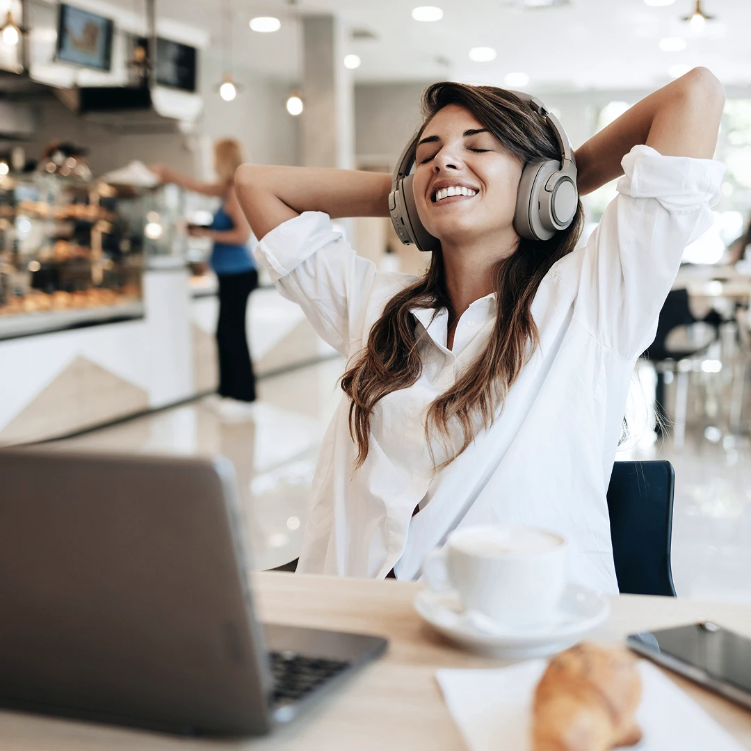 A smiling woman with brown hair wearing headphones, leaning back in a chair with her hands behind her head