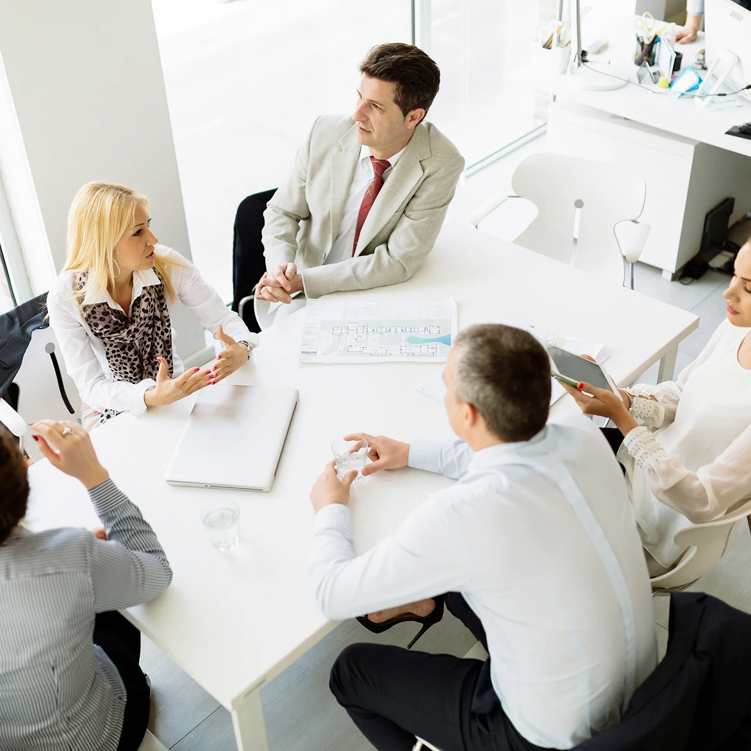 Business professionals in suits discussing around a white table in a bright office