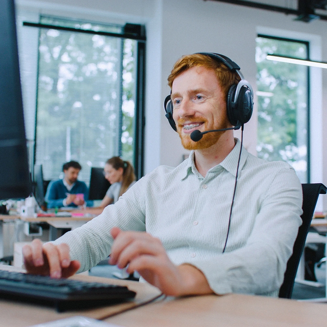 Smiling red-haired male customer support agent working at a computer in a modern Seattle call center