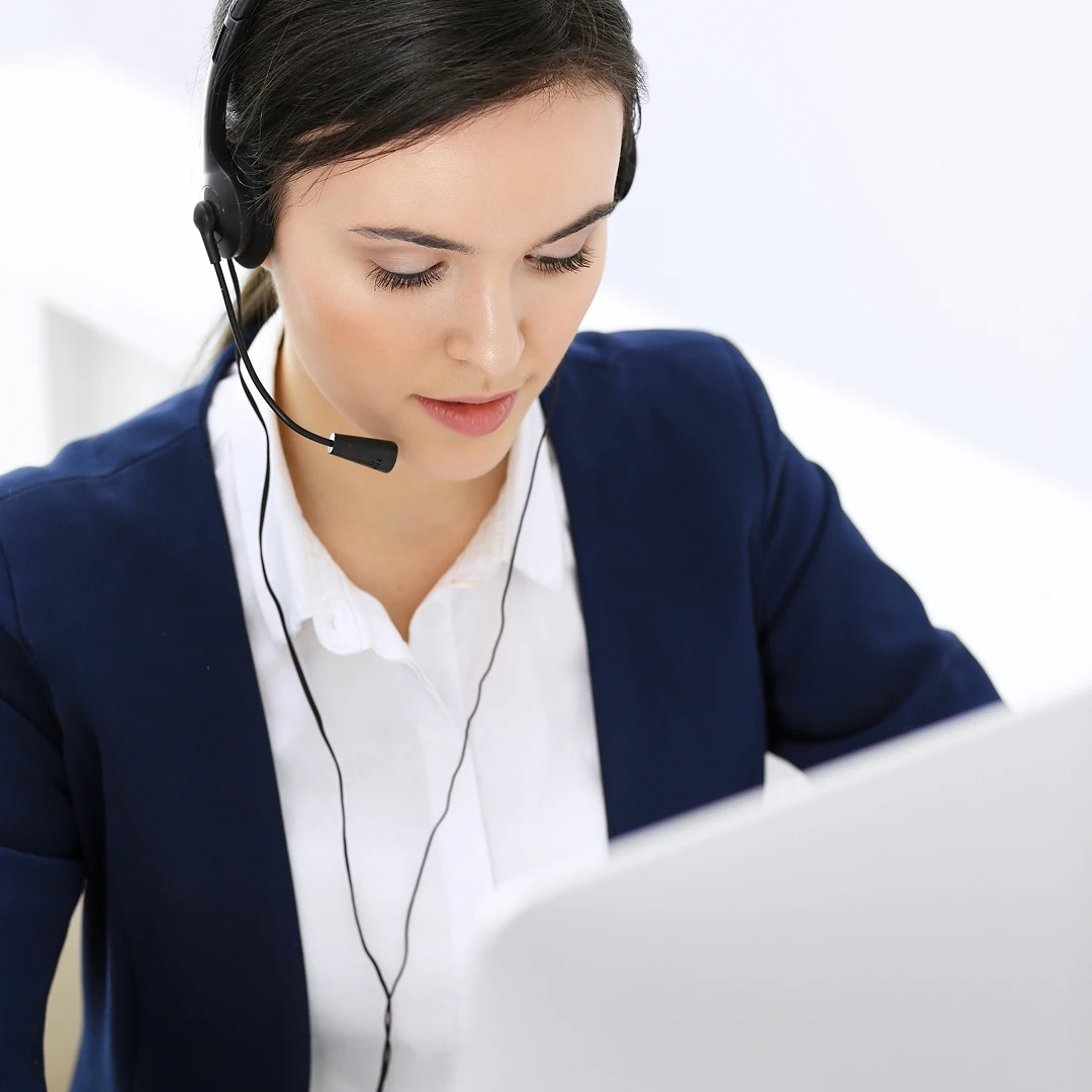 Focused female customer support agent wearing a black blazer with a white shirt and headset, working at a workstation