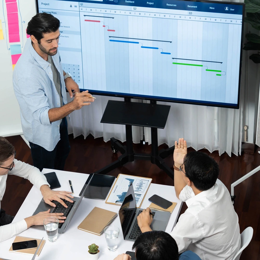 Team business meeting with people gathered around a table, discussing graphs on a large screen
