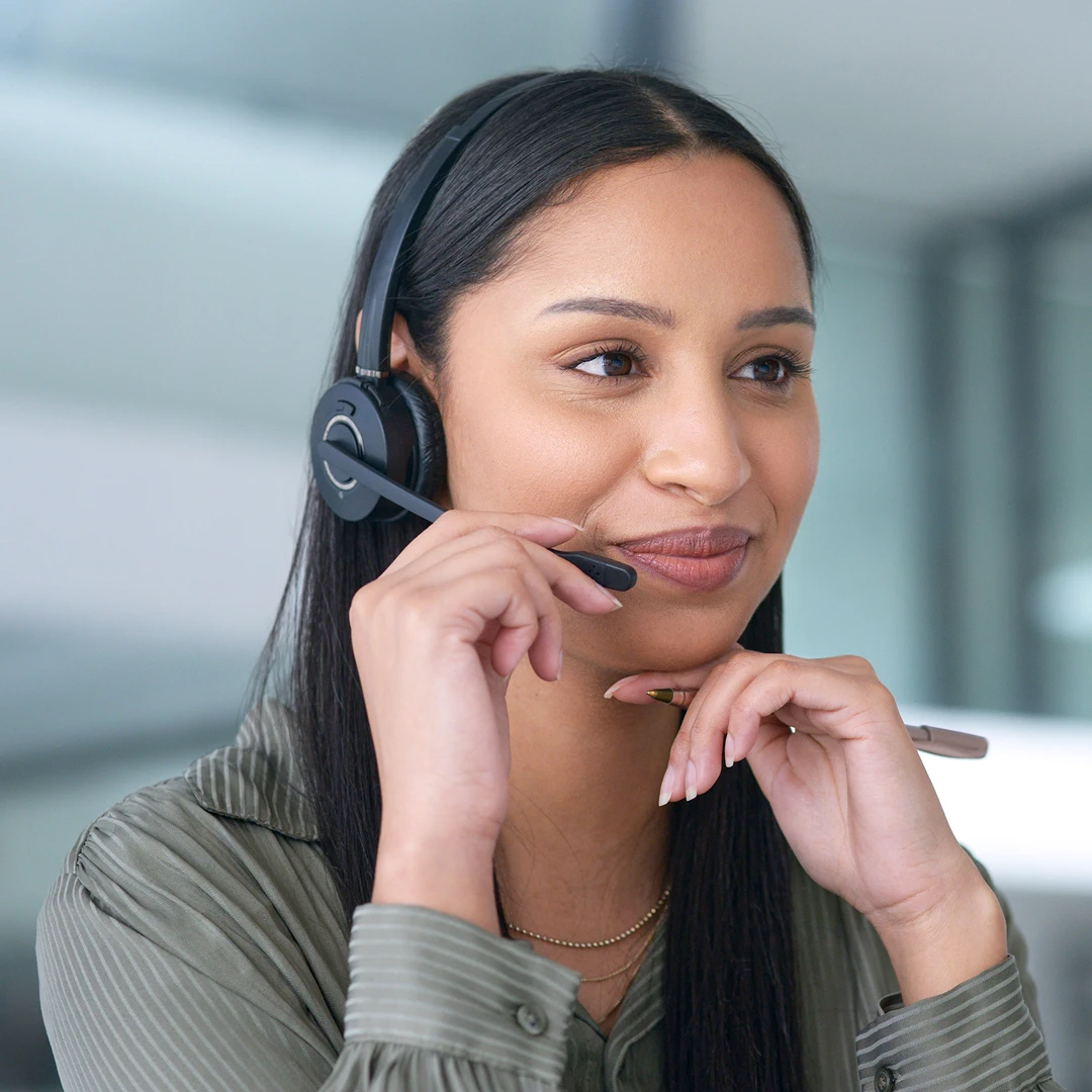 Smiling female customer support agent in olive green shirt with headset and pen in hand