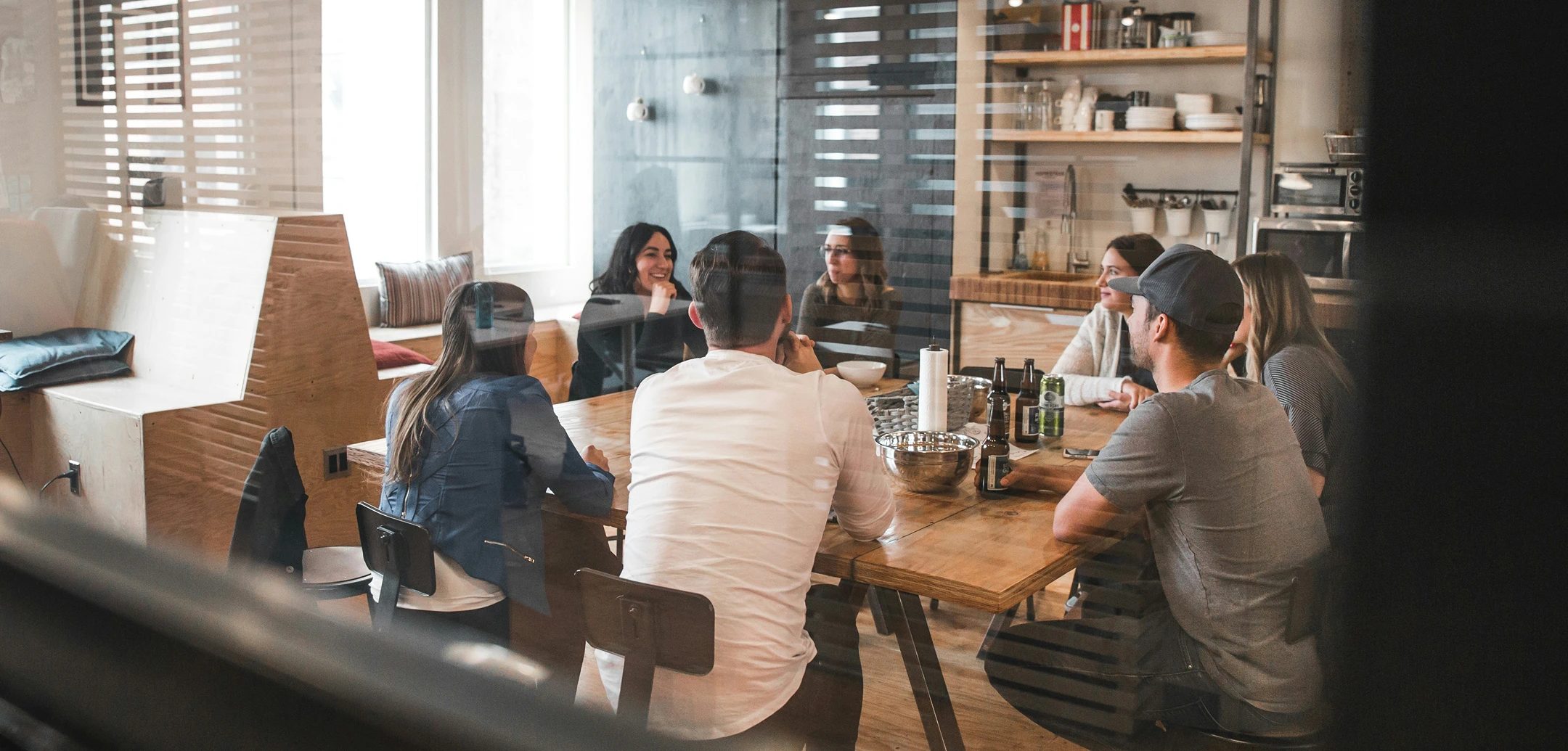 Colleagues are sitting at a wooden table in the kitchen of a modern, bright office