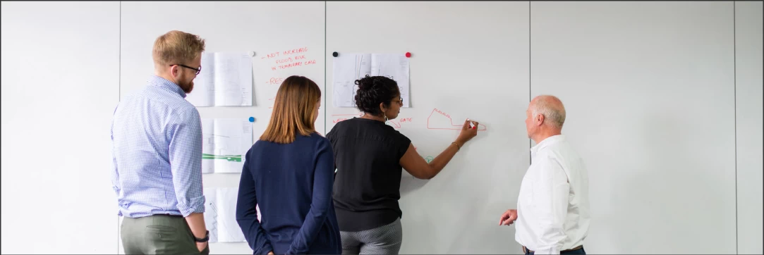 a group of people, one lady drawing something on a wall with a red marker