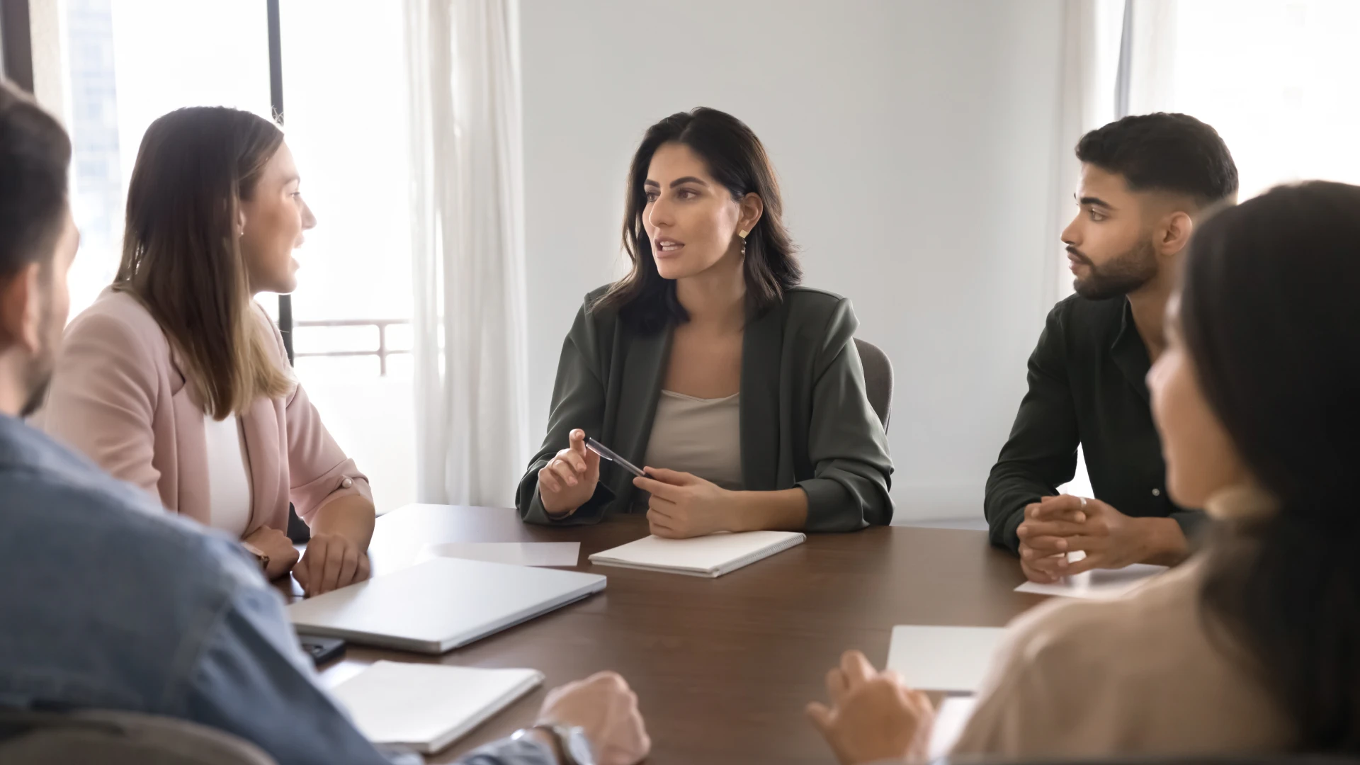 A woman in a blazer is leading a meeting with colleagues around a conference table