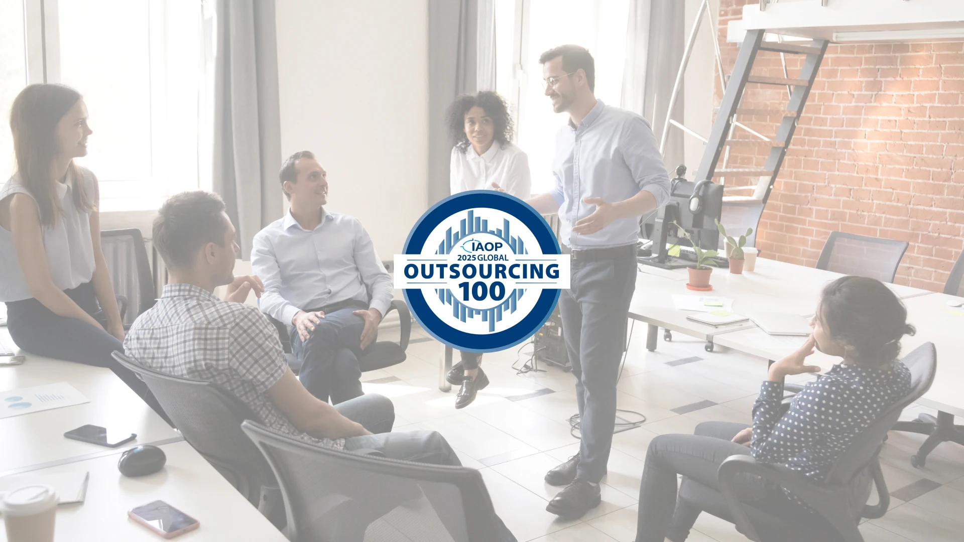 A team meeting in a bright, modern office, with one man standing and speaking to the group