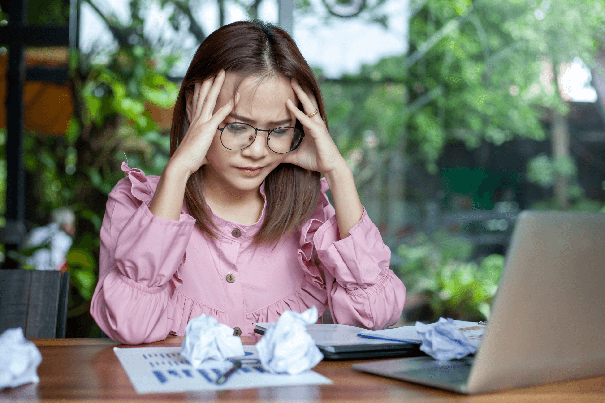 Woman in glasses with her hands on her temples, looking stressed.
