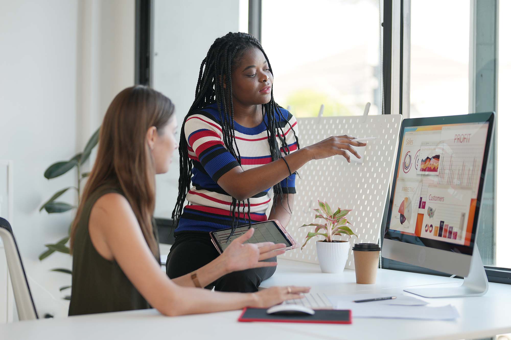 Two women are seated at a table, reviewing the audience’s sentiment analysis for their retail brand on the computer screen.