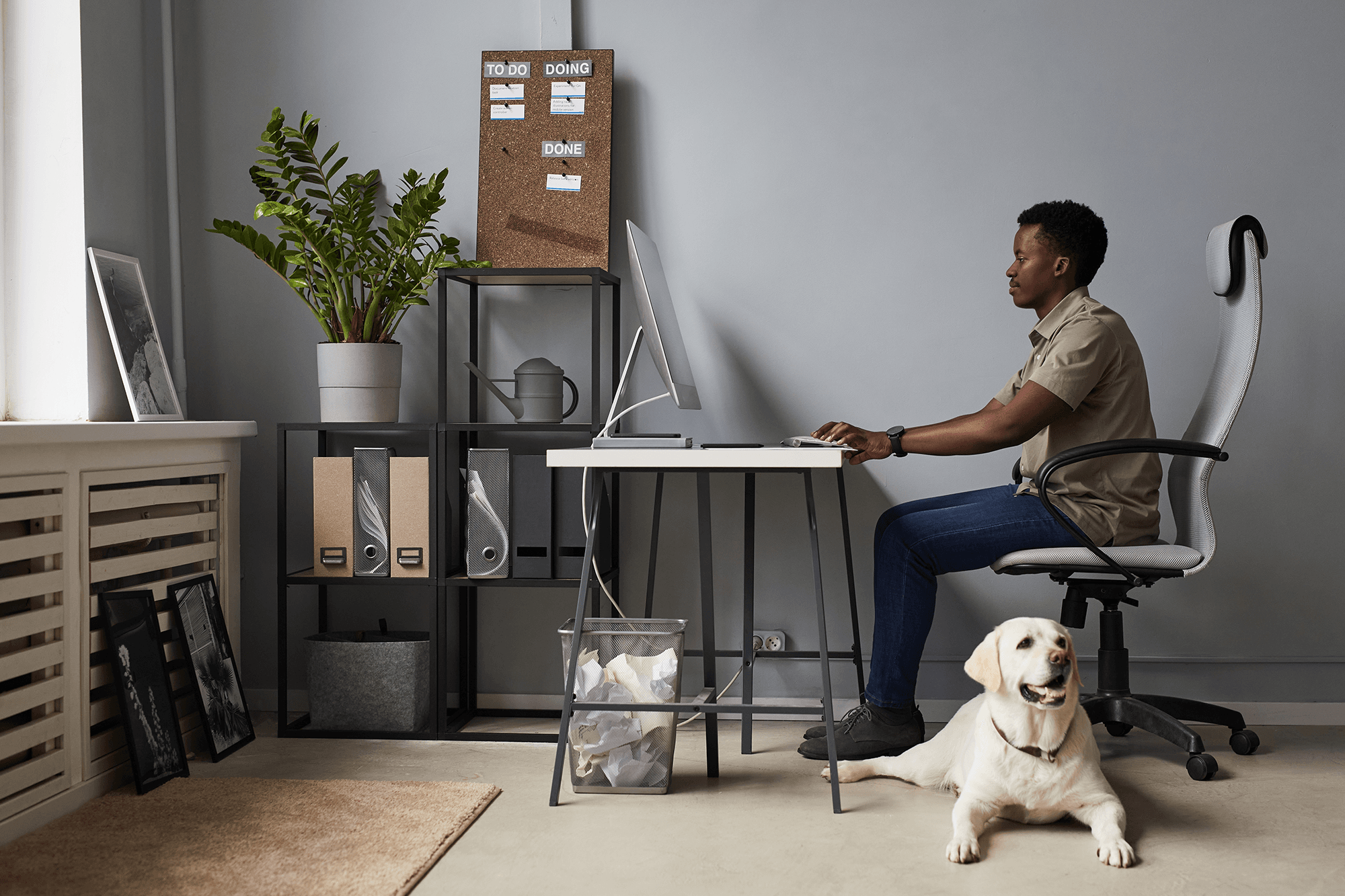 A person working remotely at their own comfortable workstation. A white Labrador Retriever is resting on the floor.
