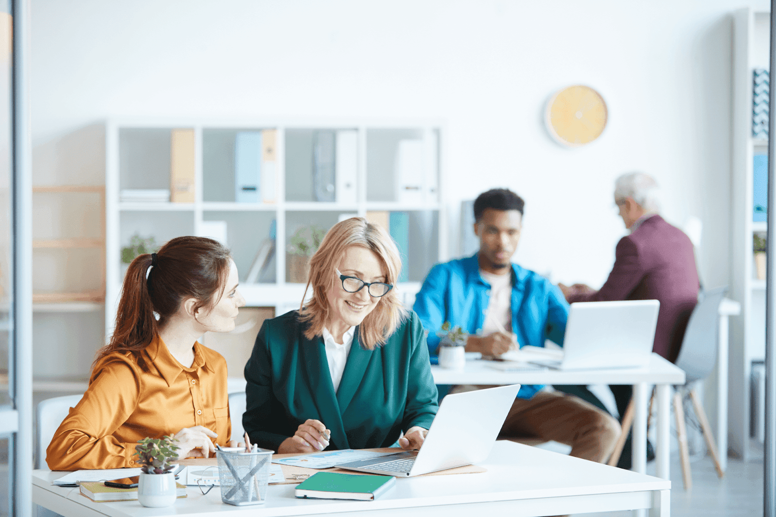 A group of professionals is collaborating at a desk in a bright office, looking at a laptop screen and discussing.