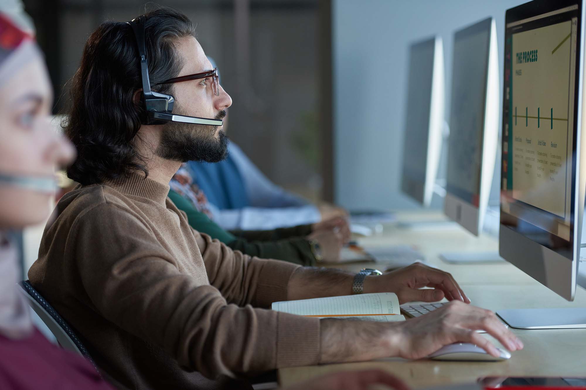 A group of call center employees working in an office, wearing headsets and focusing on their computers.